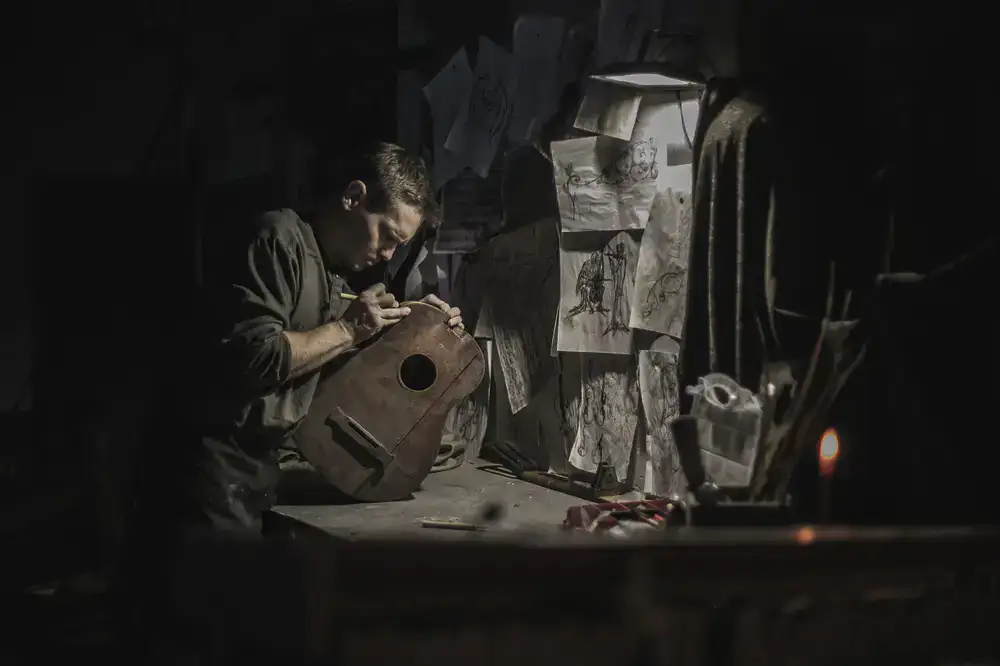 Craftsman working on a detailed wooden marionette under warm stage lighting
