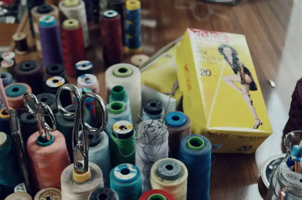 Spools of strong thread, folded fabrics, and wood blocks on a well-used workshop desk